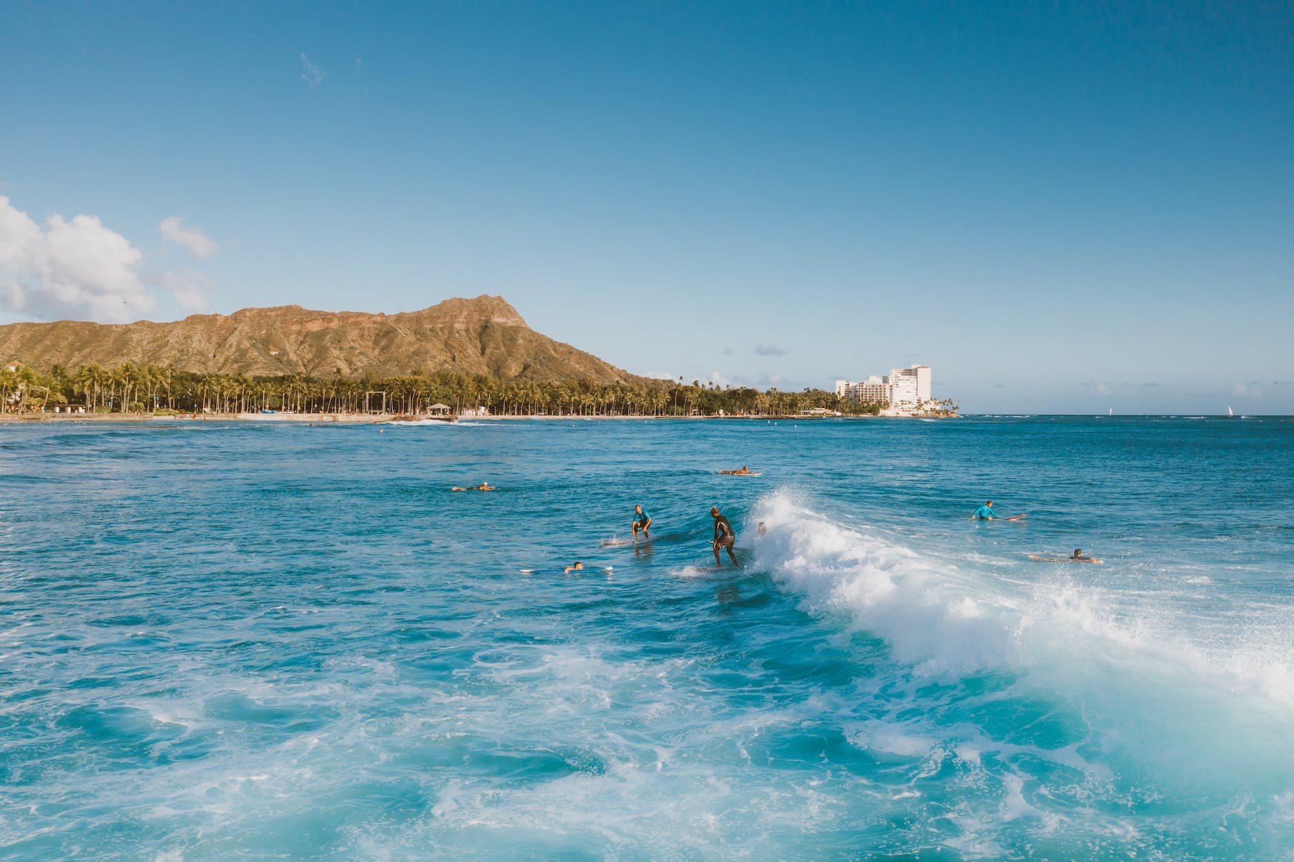 people surfing on sea near mountain under blue sky